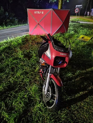 pora nocna. Przy jezdni na pasie zieleni jest rozstawiony czerwony parawan straży pożarnej. Za parawanem stoi motocykl