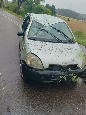 na jezdni stoi srebrna toyota yaris z wgniecionym przodem, dachem, popękaną szybą i fragmentami trawy na zderzaku