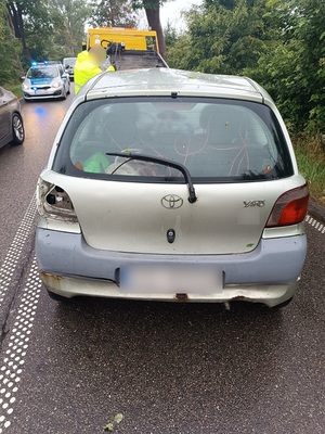 na jezdni stoi srebrna toyota yaris. Przed nią znajduje się laweta. Po drugiej stronie jezdni stoi policyjny radiowóz z włączonymi sygnałami błyskowymi