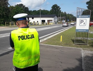 policjant ruchu drogowego za pomocą ręcznego miernika prędkości mierzy prędkość jadących ulicą samochodów