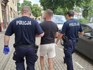 dwaj policjanci prowadzą zatrzymanego mężczyznę w kierunku nieoznakowanego radiowozu