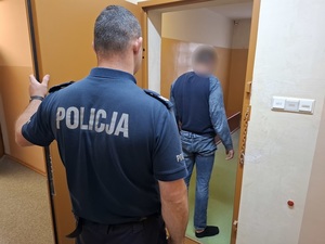 w celi stoi mężczyzna. Za nim przy otwartych drzwiach celi stoi policjant służby dyżurnej