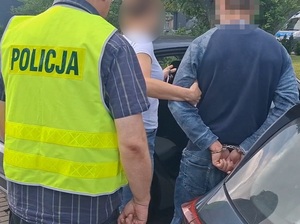 dwoje policjantów wprowadza do nieoznakowanego radiowozu mężczyznę, który ma ręce skute za plecami kajdankami