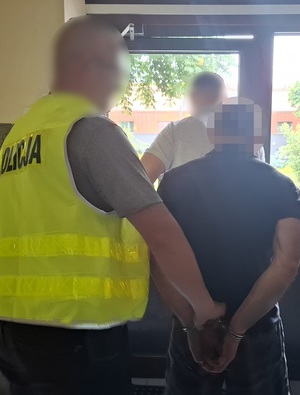 dwaj policjanci wychodzą z budynku komendy z mężczyzną, który ma ręce skute za plecami kajdankami