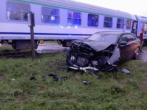 przed torami na których znajduje się pociąg stoi czarne osobowe bmw z wgniecionym przodem