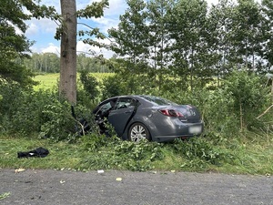 miejsce wypadku drogowego. Na poboczu znajduje się szara osobowa mazda, która uderzyła przodem w drzewo.