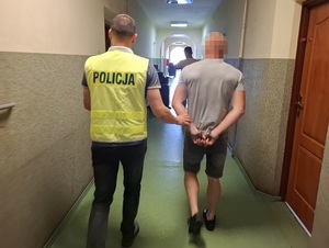 policjant prowadzi korytarzem mężczyznę, który ma ręce skute za plecami kajdankami
