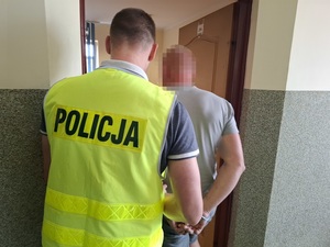 policjant wprowadza do pokoju na przesłuchanie mężczyznę, który ma ręce skute za plecami kajdankami