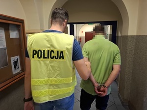 policjant prowadzi korytarzem mężczyznę, który ma ręce skute za plecami kajdankami