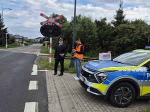niestrzeżony przejazd kolejowy. Przed przejazdem obok oznakowanego policyjnego radiowozu stoją pracownik kolei i funkcjonariusz SOK