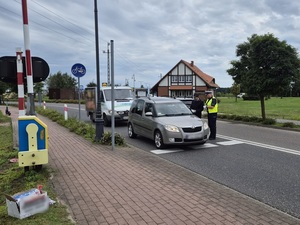 strzeżony przejazd kolejowy. Na przejeździe stoi osobowy samochód. Przy tym aucie od strony kierowcy stoją policjantka i pracownik kolei