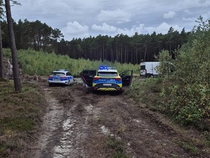na leśnej drodze gruntowej stoją dwa radiowozy, przed nimi stoi biały fiat ducato