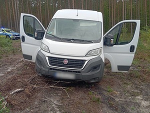 na leśnej drodze gruntowej stoi biały fiat ducato z otwartymi szeroko drzwiami. Za nim znajduje się policyjny oznakowany radiowóz