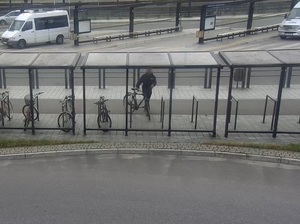 ujęcie z kamery monitoringu skierowanej na wiatę rowerową przy dworcu. W stojakach znajdują się rowery. Przy jednym stoi mężczyzna