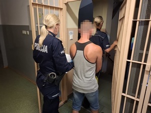 dwie policjantki wyprowadzają z okratowanego pomieszczenia zatrzymanego mężczyznę