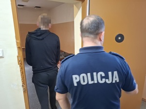 do celi wchodzi mężczyzna. Za nim przy otwartych drzwiach celi stoi policjant służby dyżurnej