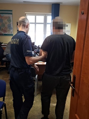 policjant wprowadza do pokoju przesłuchań zatrzymanego mężczyznę