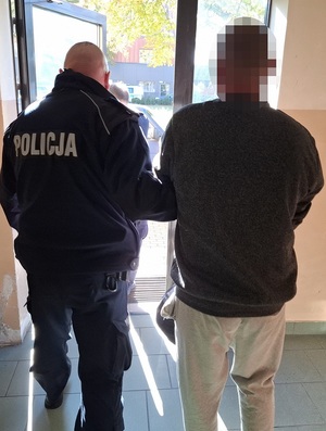 policjant wyprowadza z budynku komendy zatrzymanego mężczyznę