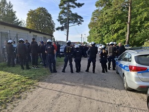 policjanci ubrani w sprzęt przeciwuderzeniowy, otaczający pseudokibiców poza ogrodzeniem stadionu, od strony sektora przyjezdnych