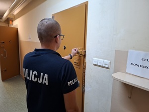 policjant służby dyżurnej zamykający zasuwę w drzwiach celi