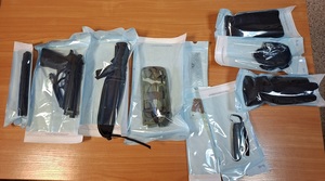 na stole leżą zapakowane w przezroczystą folię przedmioty: dwie kominiarki, nóż myśliwski w futerale, pałka teleskopowa, banknot meksykański, karta visa, pistolet, multitool, dwa przezroczyste woreczki z kulkami do pistoletu, rękawice