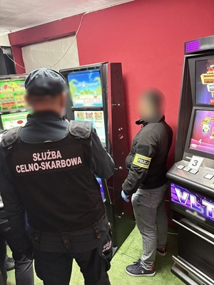 przed trzema automatami do gier stoją policjant kryminalny i funkcjonariusz służby celno - skarbowej