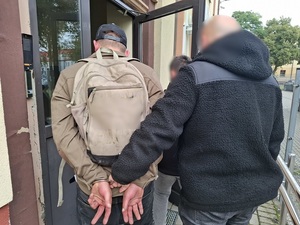 dwaj nieumundurowani policjanci kryminalni wprowadzają do budynku komendy mężczyznę, który ma ręce skute za plecami kajdankami.