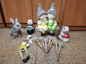 na podłodze stoją i leżą ceramiczne figurki: zając, biedronka, skrzaty siedzące na ławeczce, jeż z muchomorem, pszczółka i siedem grzybków