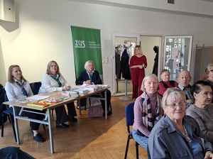 w sali klubu osiedlowego, przy ścianie obok drzwi wejściowych przy stole i rollup ZUS-u siedzą trzy przedstawicielki tej instytucji. Przed nimi na krzesłach w rzędach siedzą seniorzy