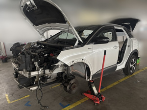 w hali na podnośniku samochodowym znajduje się osobowy biały peugeot, częściowo zdemontowany