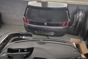 w hali pod ścianą znajduje się część tylnej karoserii szarego peugeota. Przed nią leży deska rodzielcza