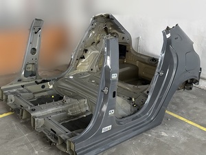 w hali na podłodze leży zdemontowana rama od szarego samochodu