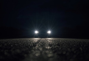 pora nocna. Na jezdni znajduje się samochód osobowy z włączonymi światłami mijania