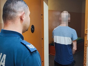 w otwartych drzwiach celi stoi zatrzymany mężczyzna. Za nim stoi policjant służby dyżurnej