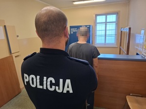 w policyjnym pomieszczeniu depozytowym stoi zwrócony tyłem do obiektywu mężczyzna. Za nim stoi policjant służby dyżurnej