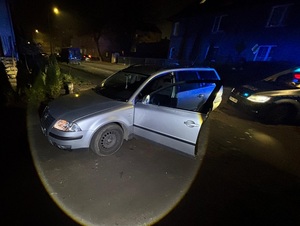 pora nocna. W mieście w poprzek ulicy stoi srebrny vw passat kombi z otwartymi drzwiami od strony kierowcy. Za nim stoi oznakowany policyjny radiowóz z włączonymi sygnałami błyskowymi