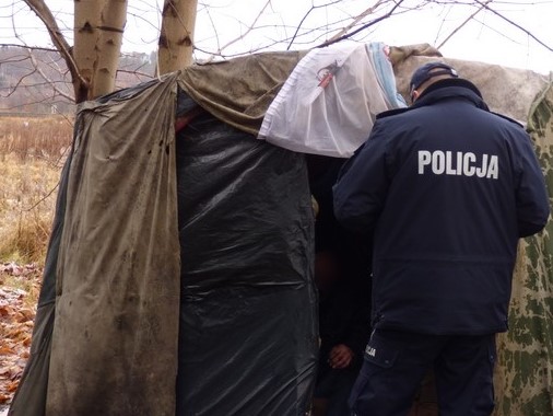 Przy prowizorycznym namiocie, zrobionym ze skrawków materiału stoi policjant