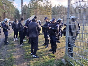 przed płotem okalającym stadion, od strony kibiców przyjezdnych, policjanci legitymują kibiców