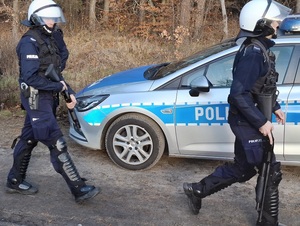 drogą od strony lasu idą dwaj policjanci trzymający strzelby gładkolufowe