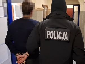 policjant kryminalny prowadzi korytarzem komendy mężczyznę, który ma ręce skute za plecami kajdankami