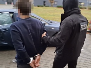 policjant kryminalny prowadzi w stronę nieoznakowanego radiowozu mężczyznę, który ma ręce skute za plecami kajdankami