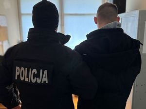 policjant kryminalny, trzymający za ramię zatrzymanego mężczyznę