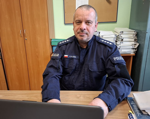 przy biurku przed laptopem siedzi policjant w umundurowaniu służbowym, w stopniu aspiranta sztabowego