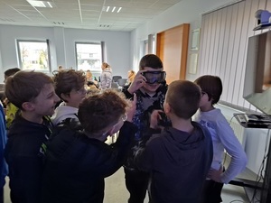 w auli lęborskiej komendy policji siedzą na krzesłach uczniowie. Przed nimi, stoi kilku chłopców. Jeden ma założone narkogogle