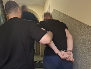 policjant kryminalny prowadzi schodami w górę mężczyznę, który ma ręce skute za plecami kajdankami