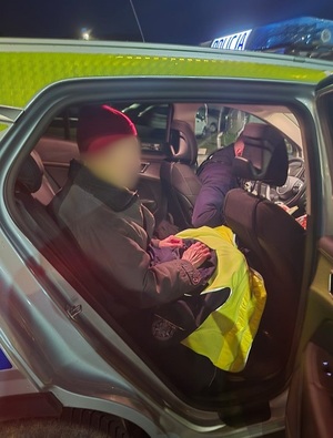 pora wieczorowa. Na tylnym siedzeniu policyjnego radiowozu siedzi starszy mężczyzna. Kolana ma nakryte policyjną kurtką