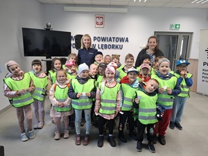 zdjęcie grupowe przedszkolaków i stojącej wśród nich uśmiechniętej policjantki. Zdjęcie zrobione w auli lęborskiej komendy Policji