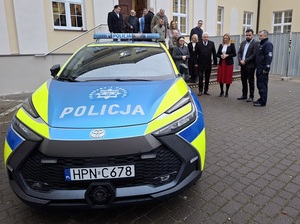 przed budynkiem lęborskiego starostwa stoi oznakowana policyjna toyota C-HR. Obok stoją przedstawiciele władz samorządowych i Komendant Powiatowy Policji w Lęborku