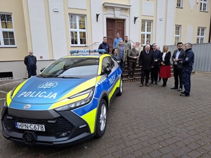 przed budynkiem lęborskiego starostwa stoi oznakowana policyjna toyota C-HR. Obok stoją przedstawiciele władz samorządowych i Komendant Powiatowy Policji w Lęborku