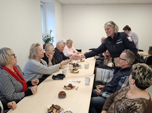 w sali przy stole siedzą seniorzy. Dzielnicowa rozdaje im odblaskowe elementy